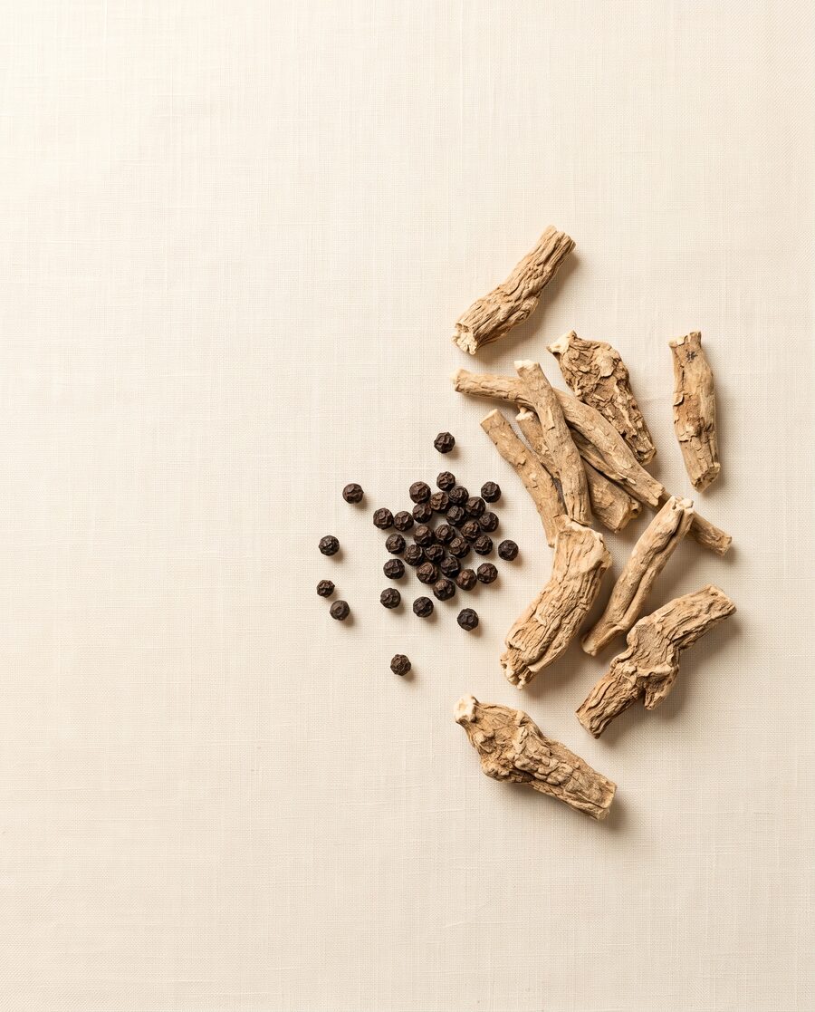Ashwagandha root pieces and black peppercorns on cream linen — the two-ingredient formula
